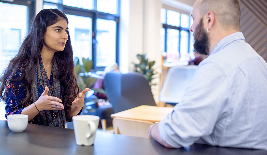 Two people in the University's Accelerator building having a face-to-face meeting with coffee