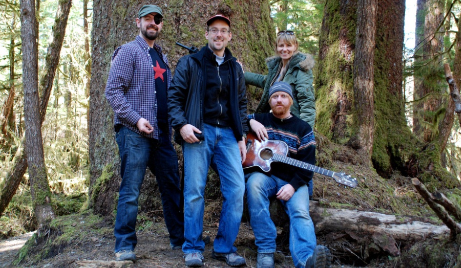 Film makers sitting under a tree in a National Forest, holding guitar, smiling. The Tongass Forest, Alaska.