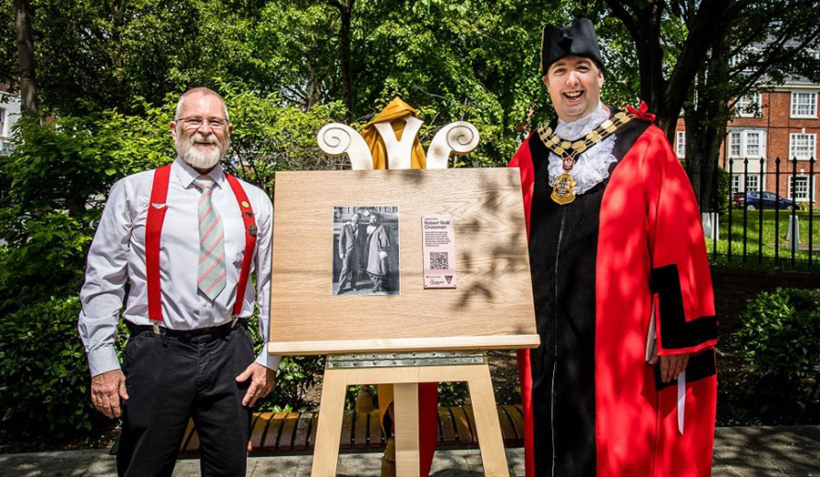 mayor, wearing red robes and a black hat, unveiling plaque