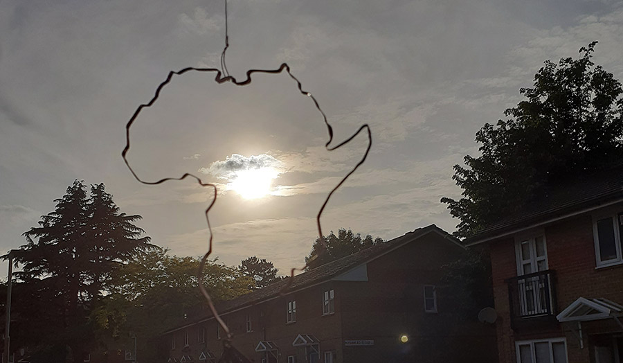 A silhouette of Africa hangs from a thin rope in a window pane with a sunset behind