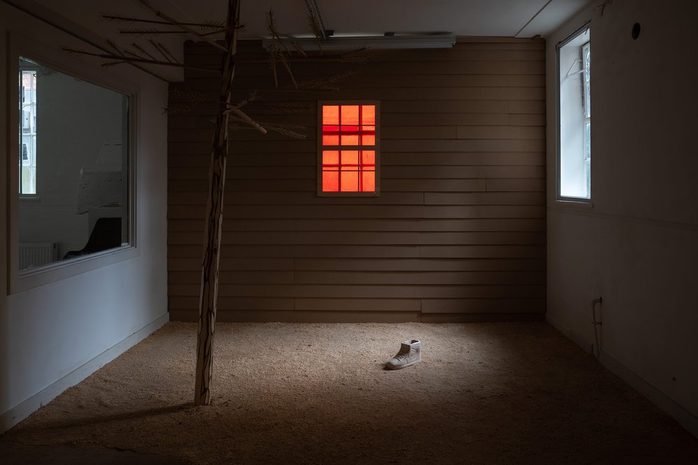 A strange dark room with small windows on both sides of the walls and in the middle of the floor there is a single boot