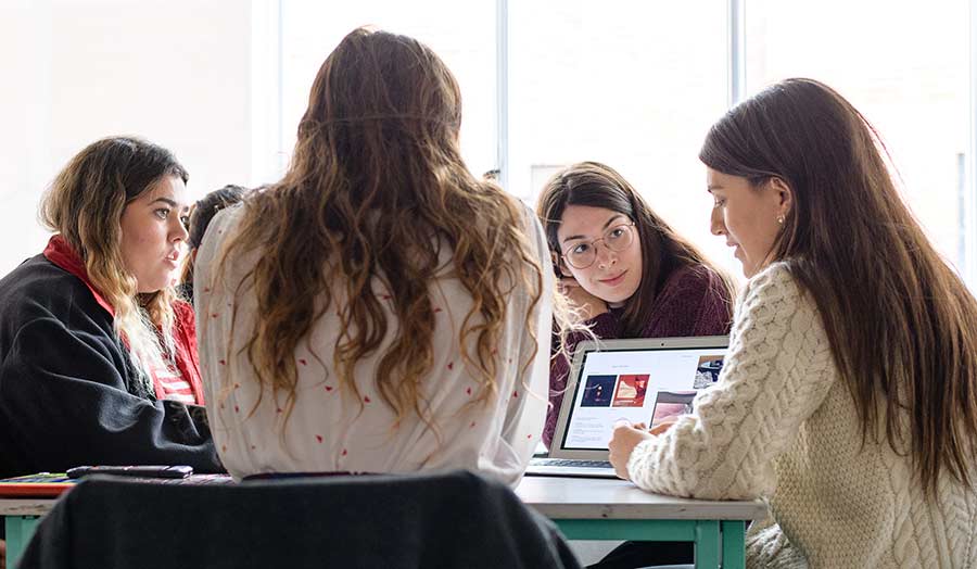 Some women sitting around the table and looking at a laptop screen