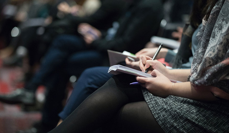 A cropped image of a people sitting in a row taking notes
