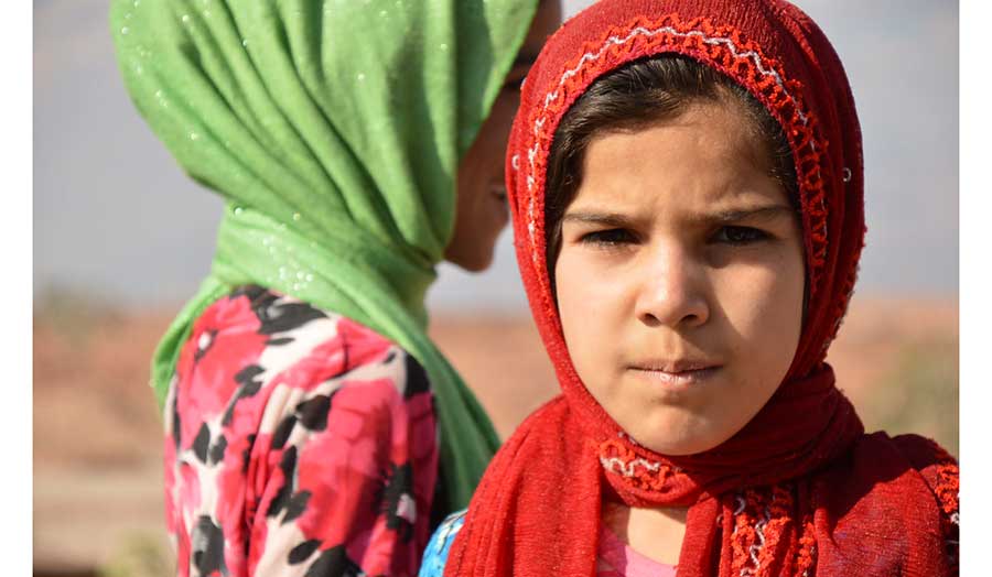 Two Afghan girls in colourful headscarfs one facing and other with her face side to the camera